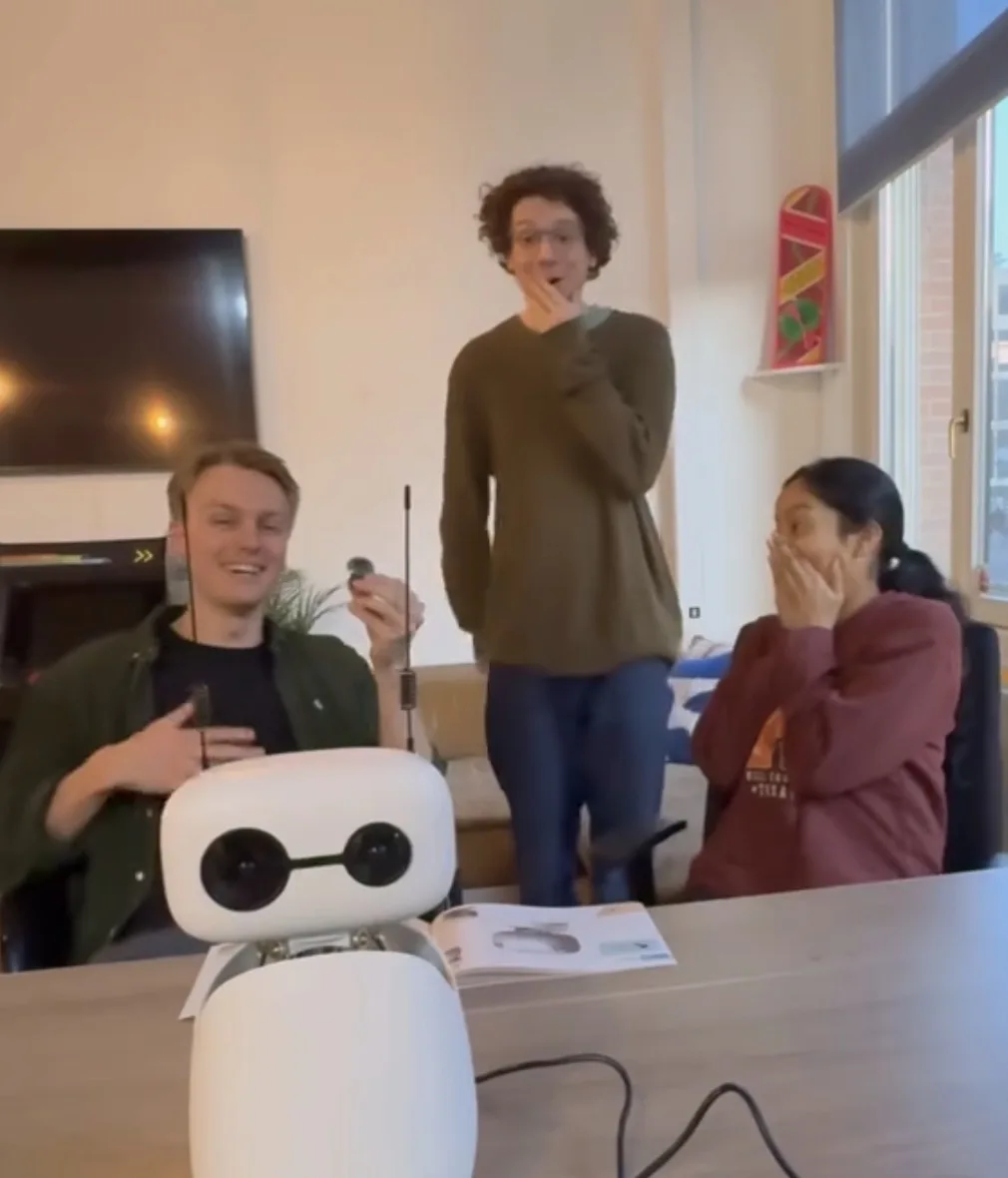 The team around a table reacting to a small white robot